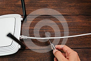 A man with a knife cuts a LAN cable connected to a router on a dark wooden background.