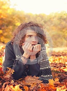 Man in knit sweater and scarf lying on autumn leaves, oudoor in autumn park. photo