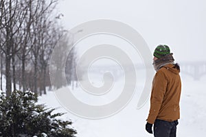 Man in knitted hat and scarf in fitness jacket staying in the snow background in the park in winter