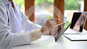 A man in a lab gown is holding and operating a tablet, A medical professional in a lab gown is using a tablet, side shot photo