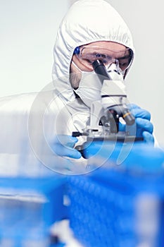 Man laborant in ppe suit using microscope doing research