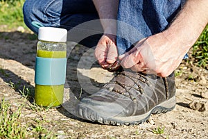 Man lacing his shoes on a walk, bottle with green smoothie made of vegetables and fruit, Healthy lifestyle, Harmony with nature