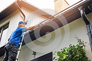 Man on ladder cleaning house gutter