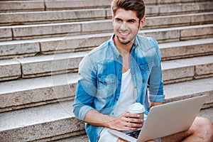 Man with laptop drinking take away coffee on the staircase