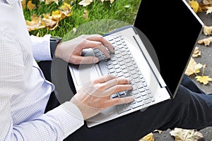 A man with a laptop on the grass in the autumn