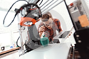 A man with a laptop in his hands controls the process of printing a 3d printer. 3d printer has printed model of an apple