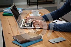 Man with laptop learning at wooden table indoors, closeup