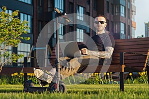 Man with laptop and modern electric kick scooter sitting at contemporary park