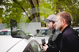 Man with a laptop in parking lot in yard near car is doing manipulations with cyber system, concept.