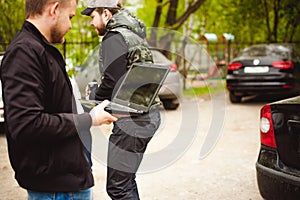 Man with a laptop in parking lot in yard near car is doing manipulations with cyber system