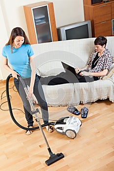 Man with laptop resting over sofa while girl doing house clean