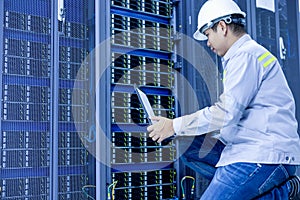 A man with a laptop sits in the server room of the data center. The system administrator works near the racks with the servers