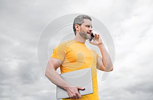 man with laptop speaking on mobile phone on sky background