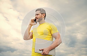 man with laptop speaking on mobile phone on sky background