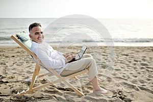 Man with laptop working on the beach sitting on a deckchair