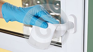 Man in latex gloves cleaning window handle with wet wipe indoors, closeup. Protective measures