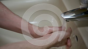 Man lathers his hands with soap under the running water of the bathroom sink