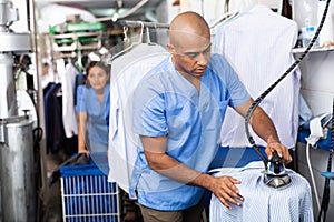 Man laundry worker ironing shirt at dry-cleaning