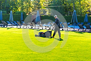 A man with a lawn mower mows grass on the lawn at a country club by the pool.