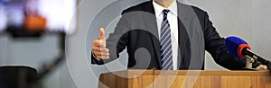 A man - a lawyer, politician or official - gestures while speaking from the podium in front of a microphone. Speaker, orator or