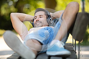 man layed on park bench listening to music through headphones