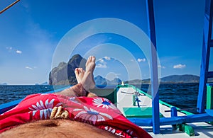 Man laying in banca boat, feet facing Inabuyatan Island by El-Nido, Palawan, Philippines