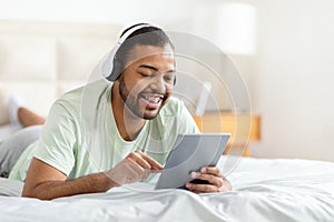 Man Laying in Bed With Headphones Using Tablet