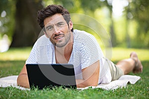 man laying down on grass and working with tablet