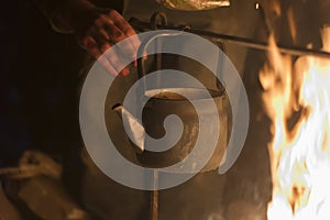 A man is laying dried herb in a kettle boiling on a fire at night