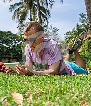 Man laying on the grass and using his tablet