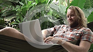 Man laying in hammock using laptop and smiling