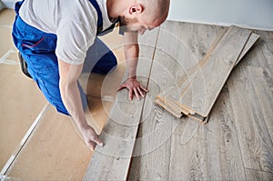 Man laying laminate wood floor in apartment under renovation.