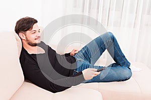 Man laying on sofa holding remote control and smiling