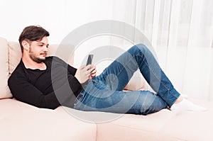 Man laying on sofa holding smartphone and texting