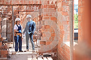 Man lead architect walking along construction site with workwoman