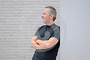 Man leaning against a wall with his arms crossed and looking expectantly