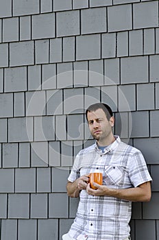 Man leaning against a wall holding a coffee mug.