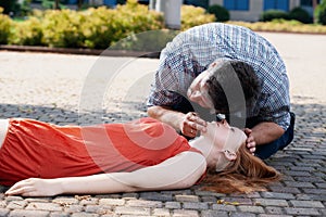 Man leaning over a woman lying on the street and checking her life functions
