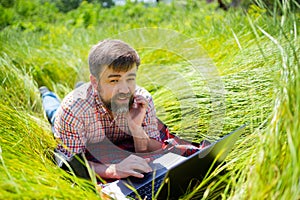 Man learns, working on laptop lying on meadow. mobile Internet in rural