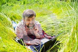 Man learns, working on laptop lying on meadow. mobile Internet in rural