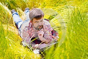 Man learns, working on laptop lying on meadow. mobile Internet in rural