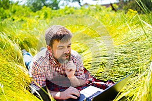 Man learns, working on laptop lying on meadow. mobile Internet in rural