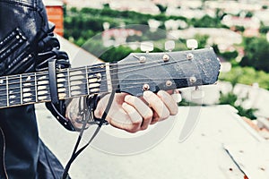 Man in a leather jacket close up tunes old black acoustic guitar