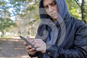 A man in a leather jacket looks at the phone in the middle of the forest. Social media immersion, orienteering, and phone stress