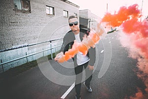 Man in a leather jacket standing at the street with smoke bomb. Colorful portrait of european teenager with red smoke bomb