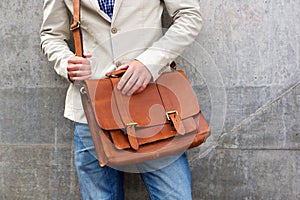 Man with leather shoulder bag standing wall