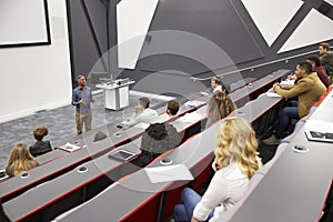 Man lectures students in lecture theatre, mid row seat POV