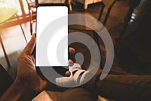 Man left hand holding mockup blank white screen cell phone and He wears sneakers with cross-legged sitting position, sit on the