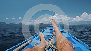 Man legs on banca boat deck on island hopping trip approaching tropical island. travel, relaxation and vacations concept