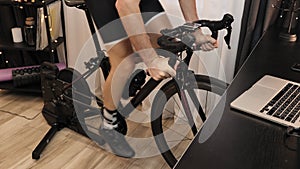 Man legs are cycling indoors on stationary bicycle. Cyclist is doing fitness cardio workout on indoor smart cycling trainer. Male